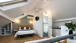 A modern hotel room with a skylight, a bed, a desk with breakfast items, and a kitchen area. - Hôtel Résidence Montebello (Paris)