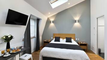 A modern bedroom with a bed, bedside tables, a desk with a chair, a flat-screen TV, and a skylight.