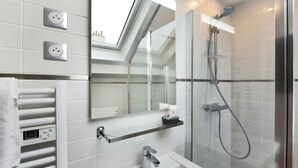 A modern bathroom with a skylight, a glass-enclosed shower, a white sink, and a towel rack. - Hôtel Résidence Montebello (Paris)