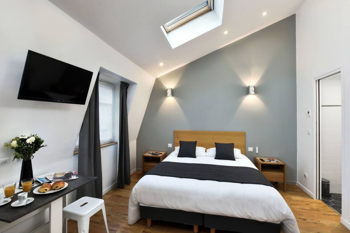 Un dormitorio moderno con cama, mesitas de noche, escritorio con silla, televisor de pantalla plana y tragaluz.