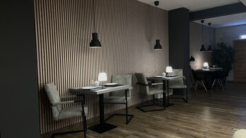 Un comedor moderno con pared de listones de madera, dos mesas con sillas e iluminación colgante.