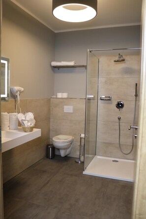 Un baño moderno con cabina de ducha de vidrio, un lavabo blanco con artículos de aseo y un inodoro.