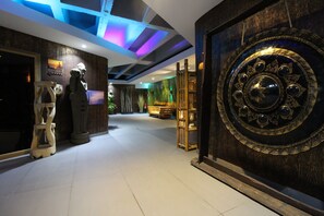 Un vestíbulo con un amplio muro decorativo, una puerta de madera e iluminación azul en el techo.