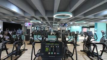 Ein Fitnessstudio mit mehreren Ergometer und Laufbändern, einem modernen Deckengestaltungsstil und einem sichtbaren Fernsehbildschirm.