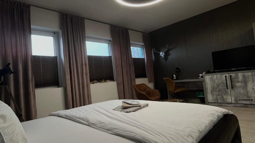 Et hotelværelse med seng, skrivebord, fjernsyn og et stort vindue med gardiner.