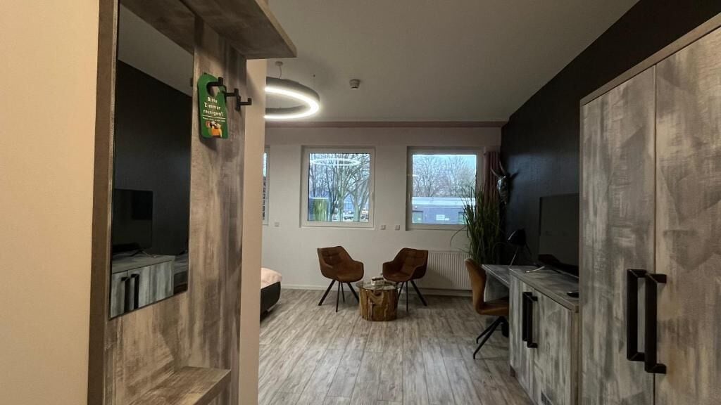 A modern kitchen with a built-in oven, a dining area with two chairs, and a large cabinet with a microwave.