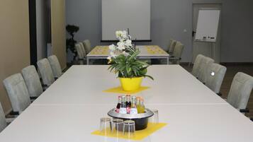 A conference room with a long table, chairs, a projector screen, a whiteboard, and a small plant.