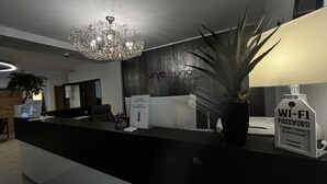 En moderne receptionsdisk med en lysekrone, en plante og et skilt, der angiver tilgængelighed af Wi-Fi kode.