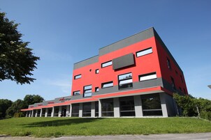 Un edificio moderno con fachada roja y gris, múltiples ventanas y techo plano.