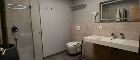 Ein modernes Badezimmer mit Duschkabine aus Glas, Toilette, Waschbecken mit Spiegel und Handtuchhalter.