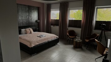 Un dormitorio moderno con una cama grande, dos sillones, una mesita y una cámara sobre un trípode.