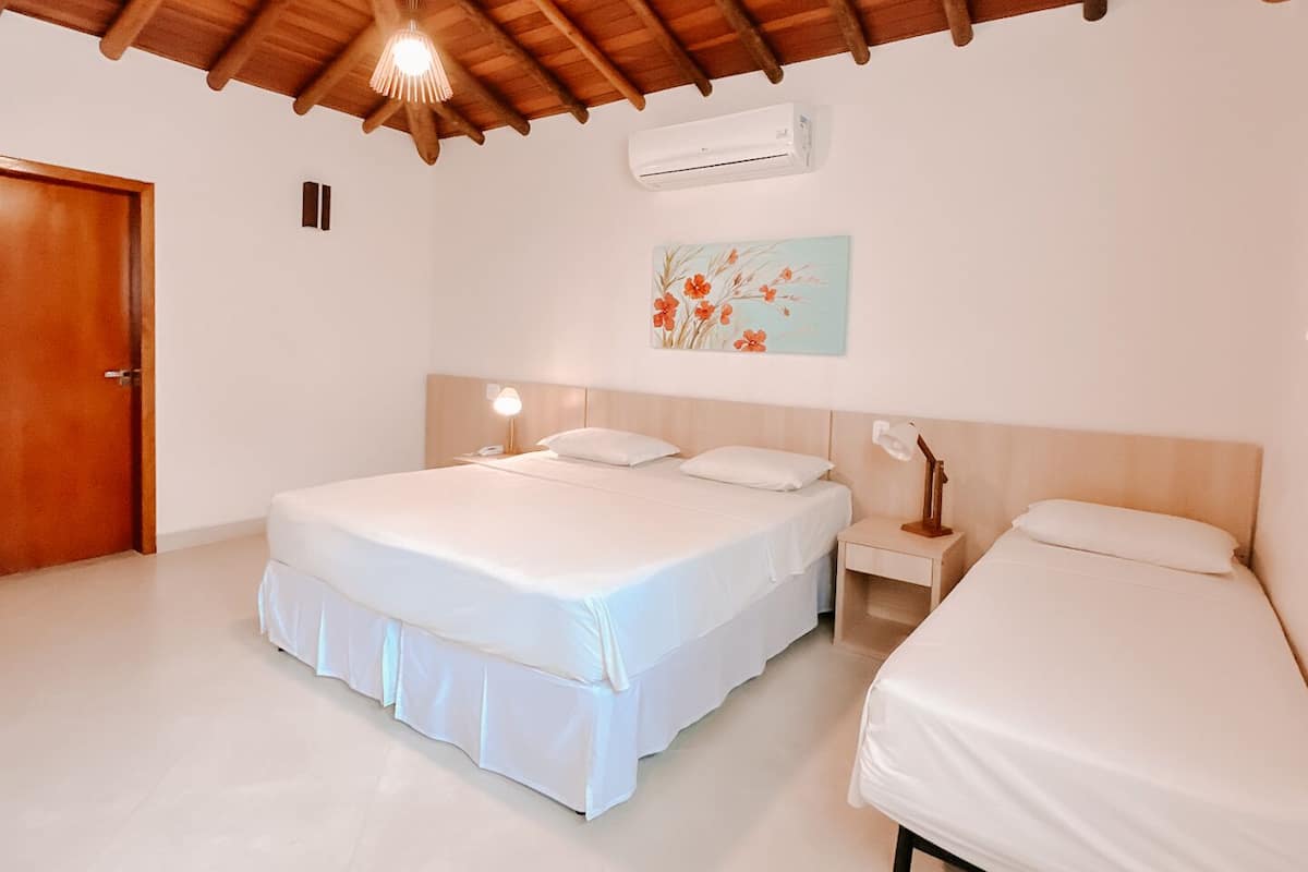 A room with two beds, a wooden ceiling, an air conditioner, a painting, and a door.
