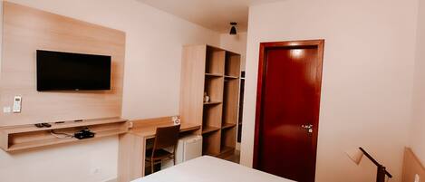 A modern hotel room with a bed, a desk, a TV, and a wardrobe.