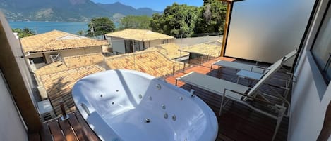 Un moderno jacuzzi al aire libre en una terraza de madera con vista a un paisaje montañoso y un cuerpo de agua.