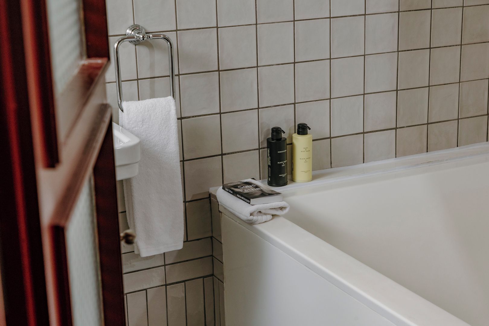 A bathroom with a bathtub, a towel rack with a white towel, and two bottles of toiletries on the edge of the tub.