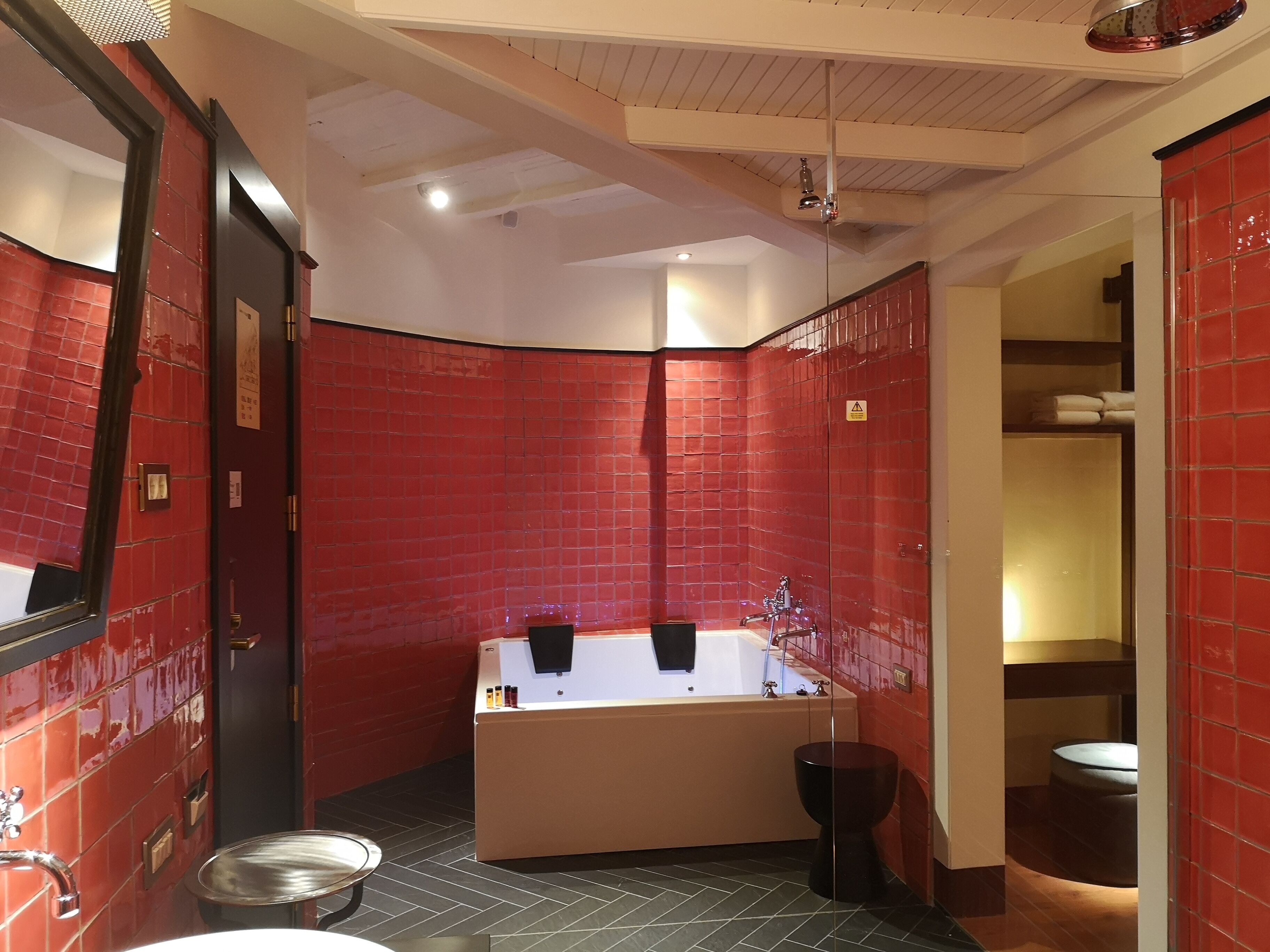 A modern bathroom with red tiled walls, a large bathtub, a sink, and a toilet.