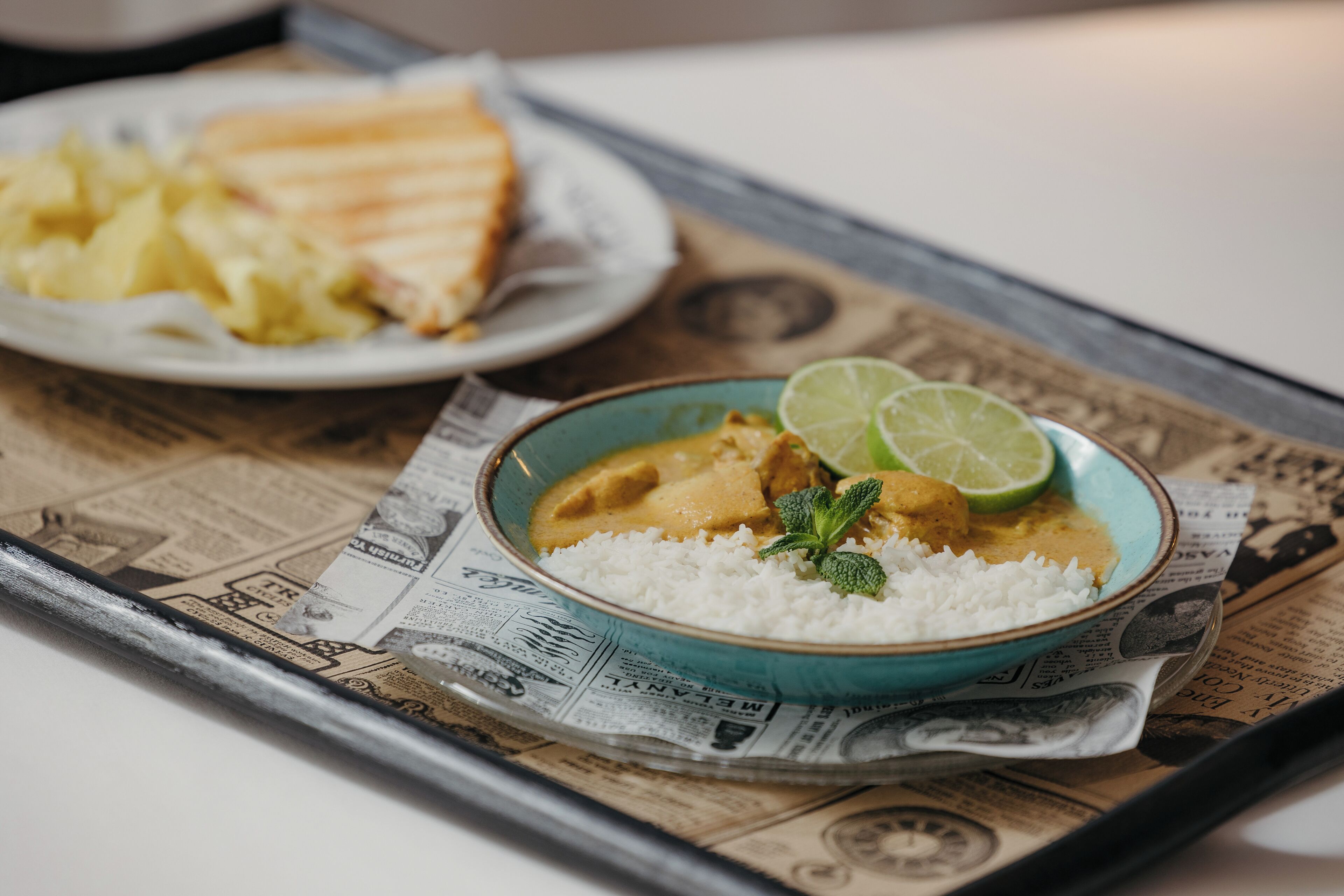 A meal with rice and a curry dish, served on a tray with newspaper.