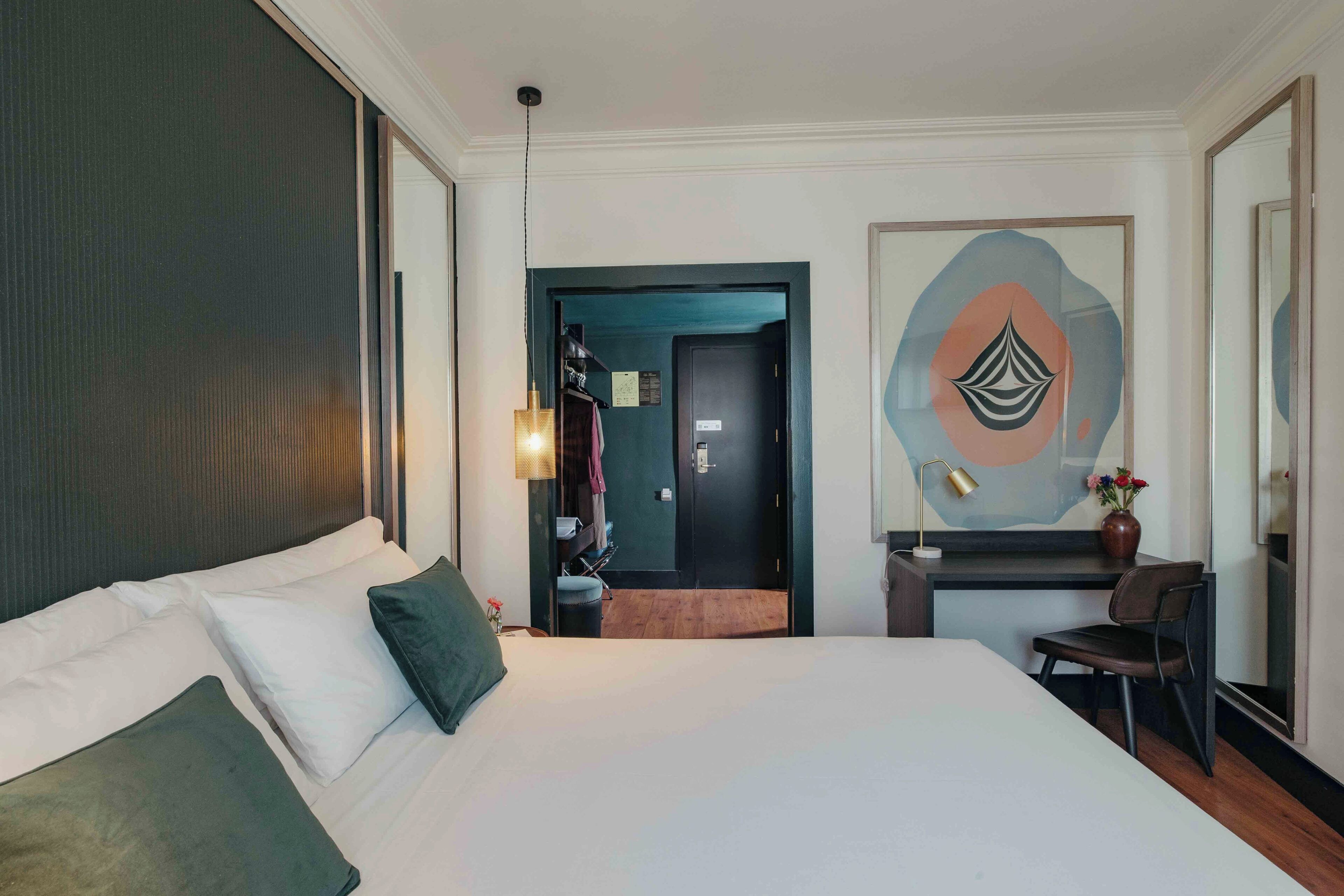A hotel room with a large bed, a desk with a chair, and a painting on the wall.