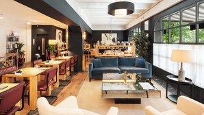 A spacious hotel lobby with a modern design, featuring a large blue sofa, multiple seating areas, a coffee table, and large windows offering a view of the outdoors. - LA FRANÇA HOTEL BOUTIQUE (Barcelona)