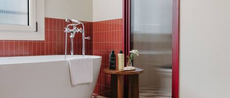A bathroom with a freestanding bathtub, a window, and a small table with toiletries.