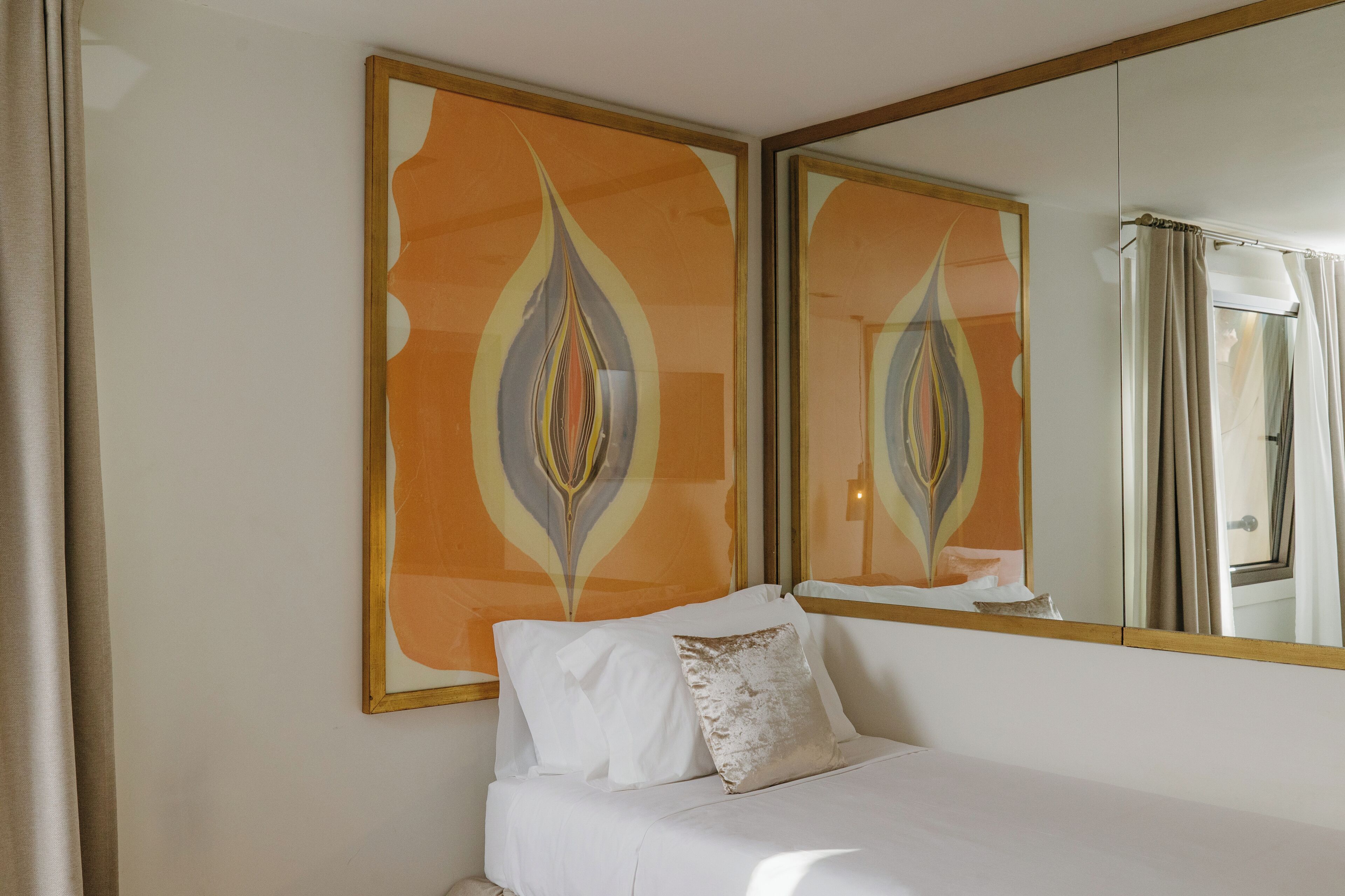 Een hotelkamer met een bed, een grote spiegel en abstracte muurkunst.