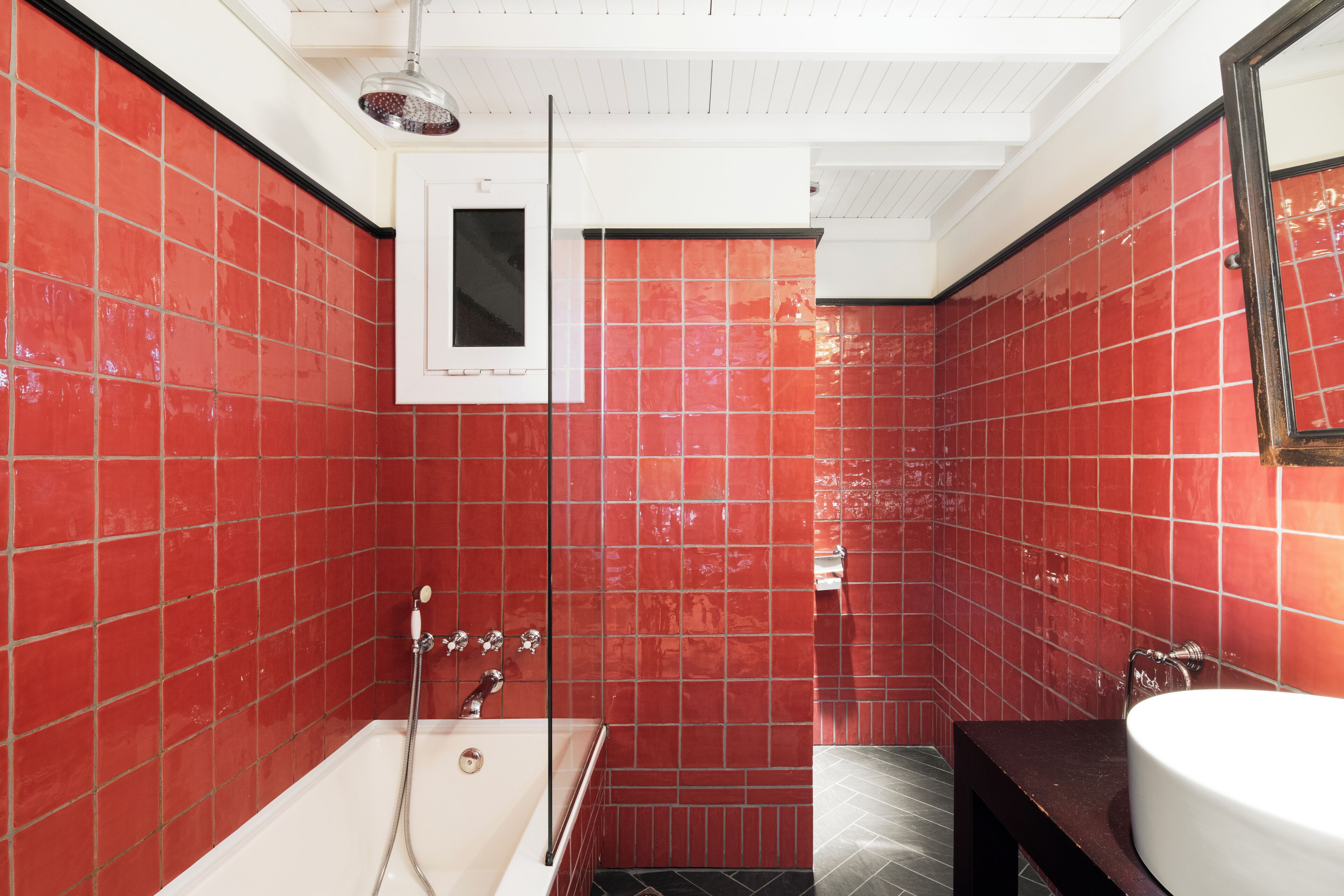 A bathroom with red tiled walls, a white bathtub, and a sink.