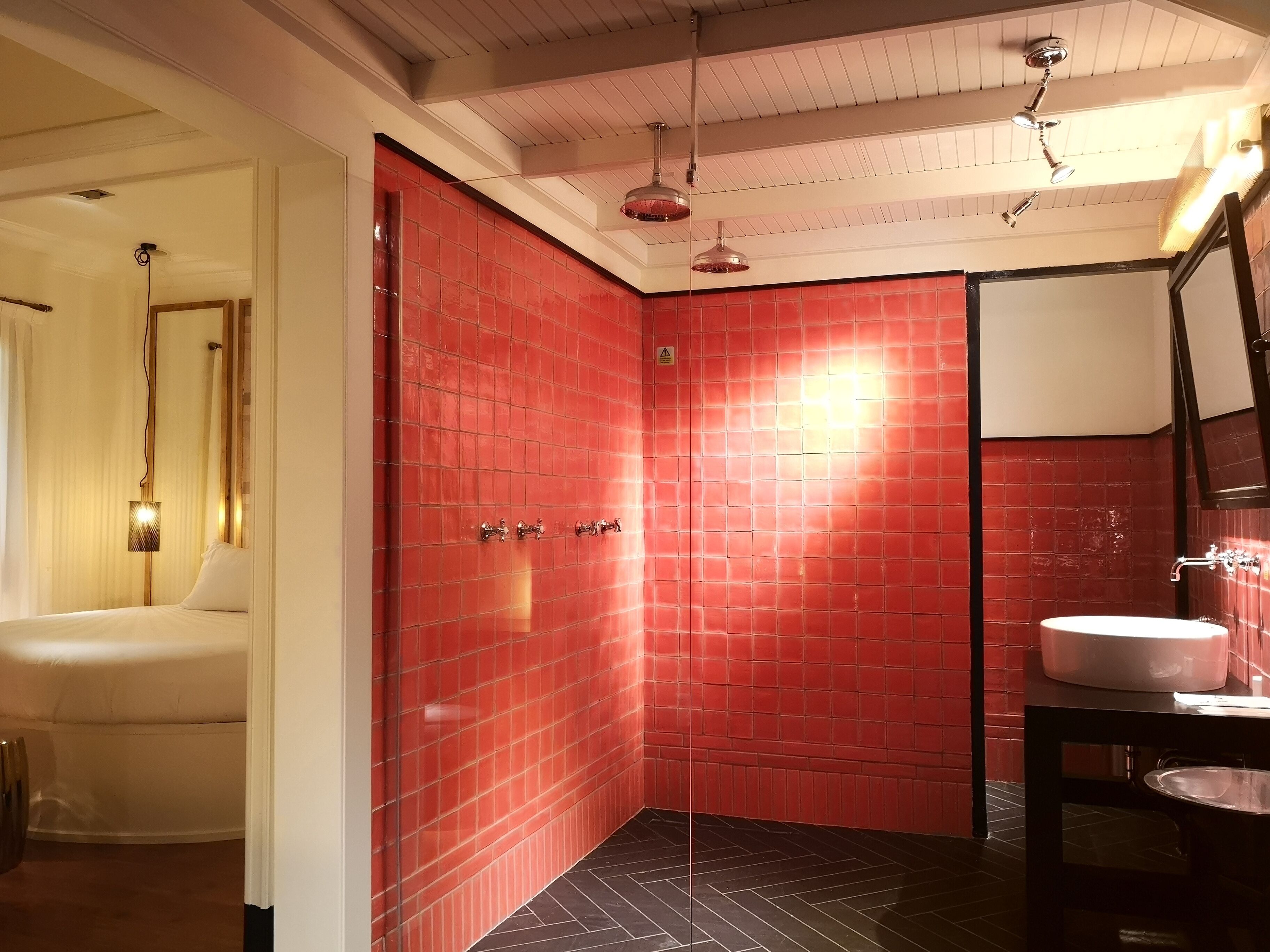 A bathroom with red tiled walls, a white sink, and a shower area.