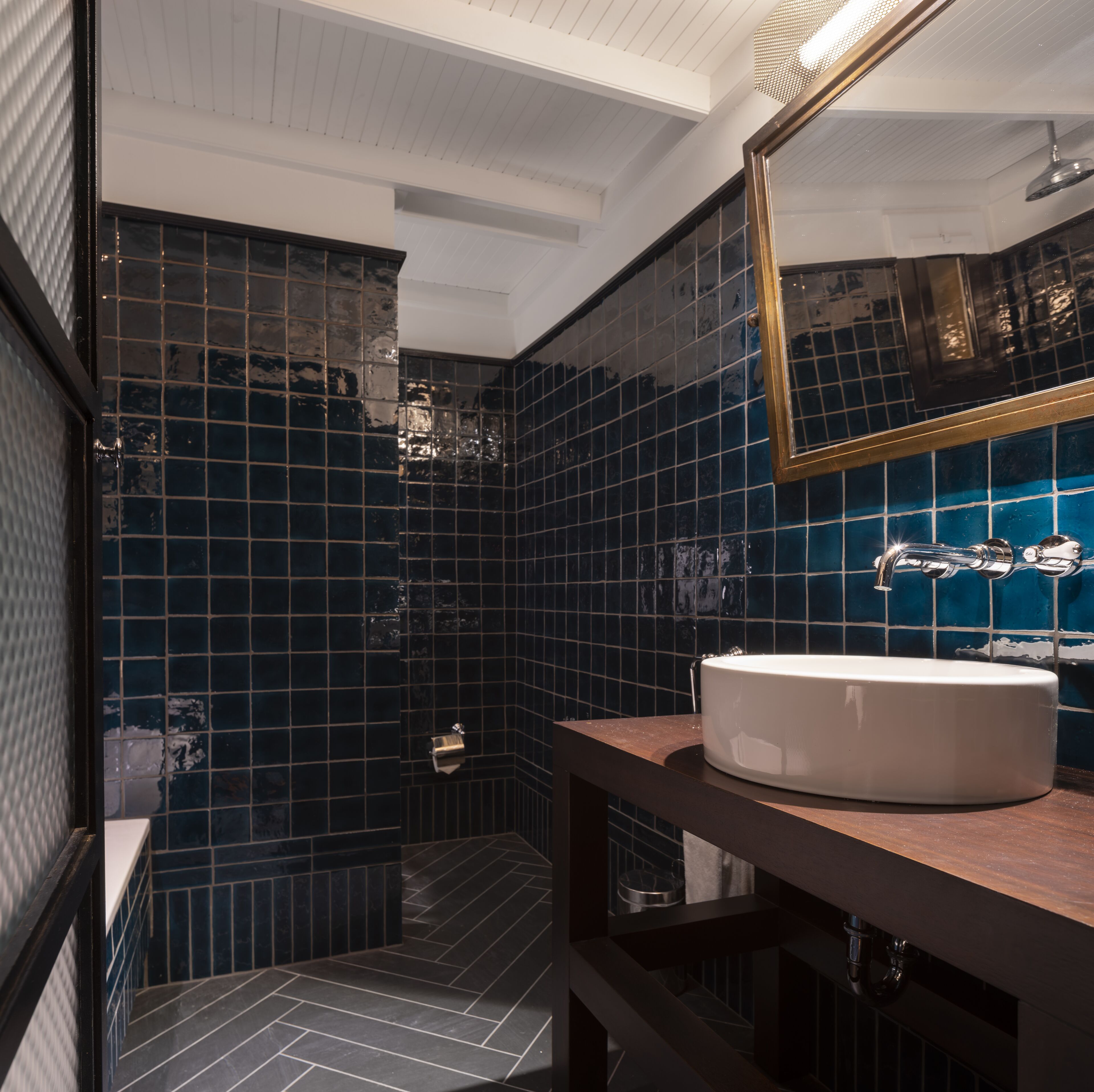 A bathroom with dark blue tiles, a white sink, and a mirror.