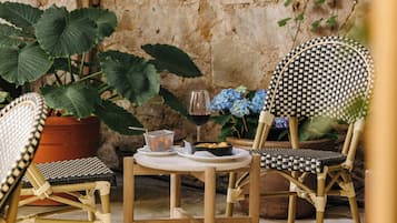 Wicker chairs, a round table, a potted plant, a glass of red wine, and a basket of oranges.