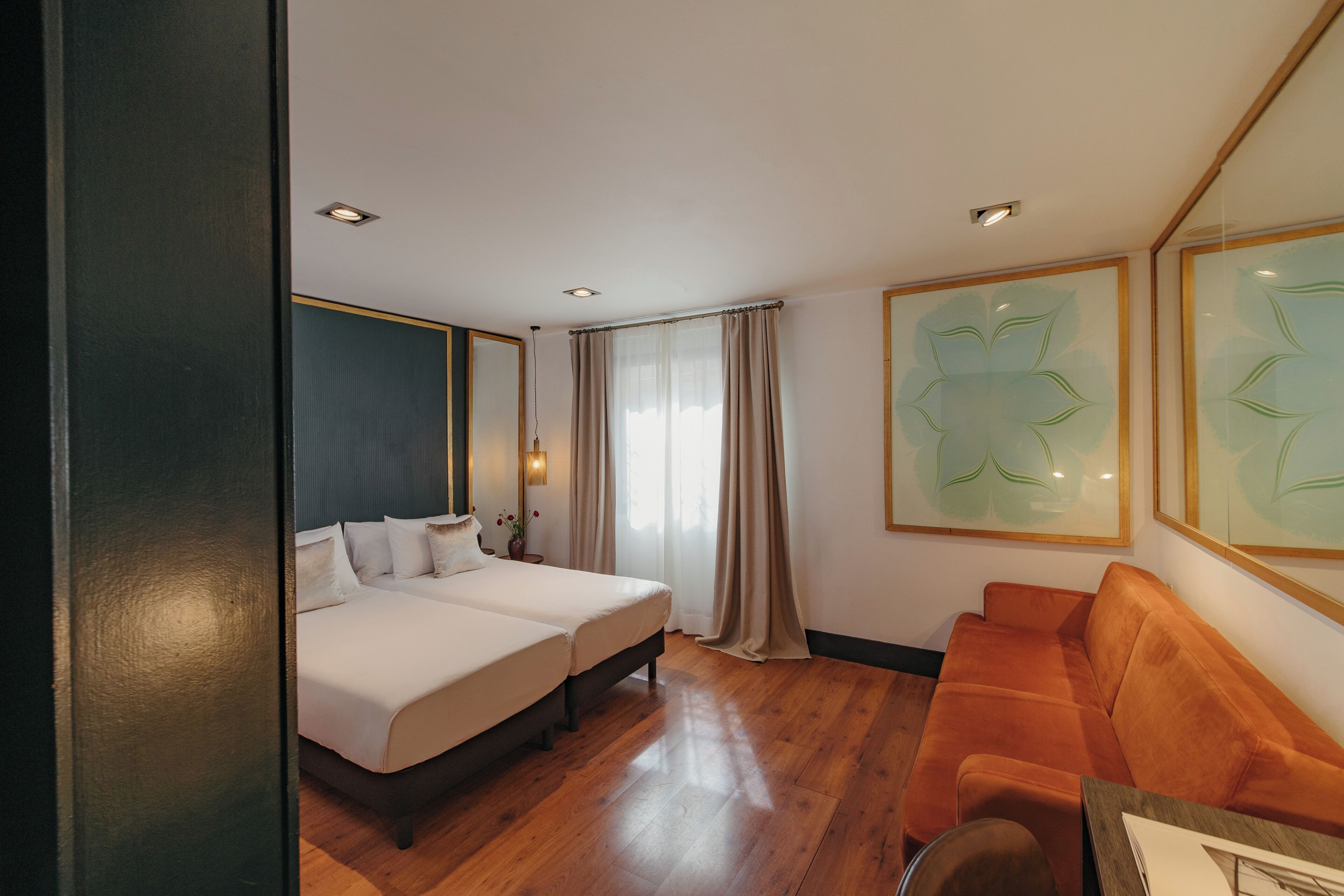 Habitación de hotel con dos camas, un sofá y un ventanal con cortinas.