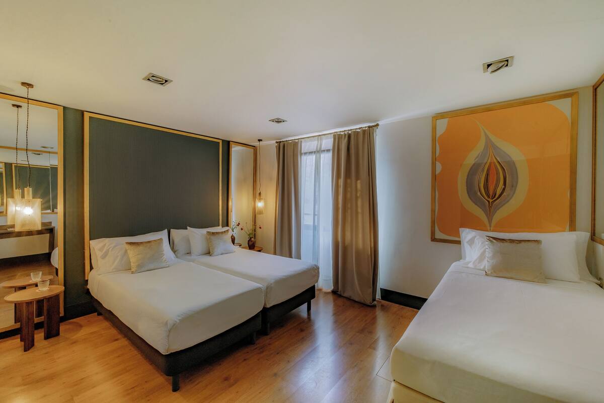 Une chambre d’hôtel avec deux lits, un coin salon avec une table et des chaises, un grand miroir et un élément décoratif mural.