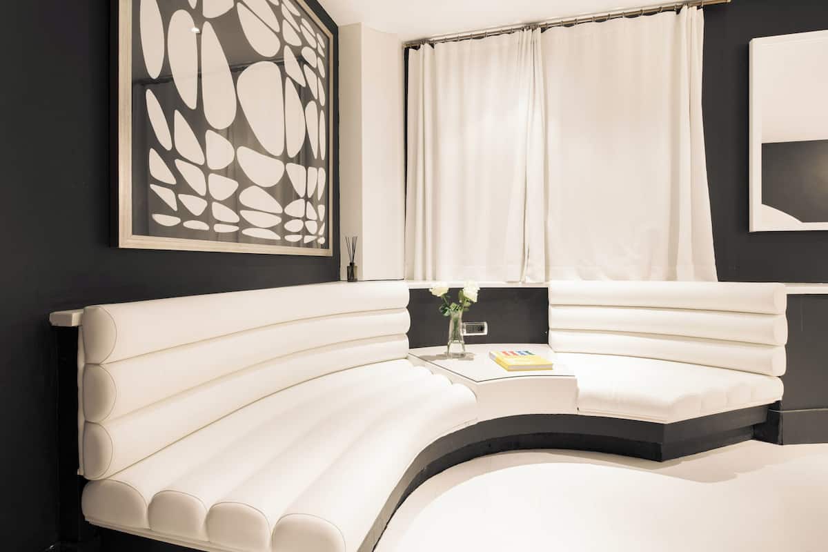 Une chambre à coucher moderne avec un lit aux lignes courbes, une grande œuvre d’art abstraite accrochée au mur et une fenêtre ornée de rideaux blancs.