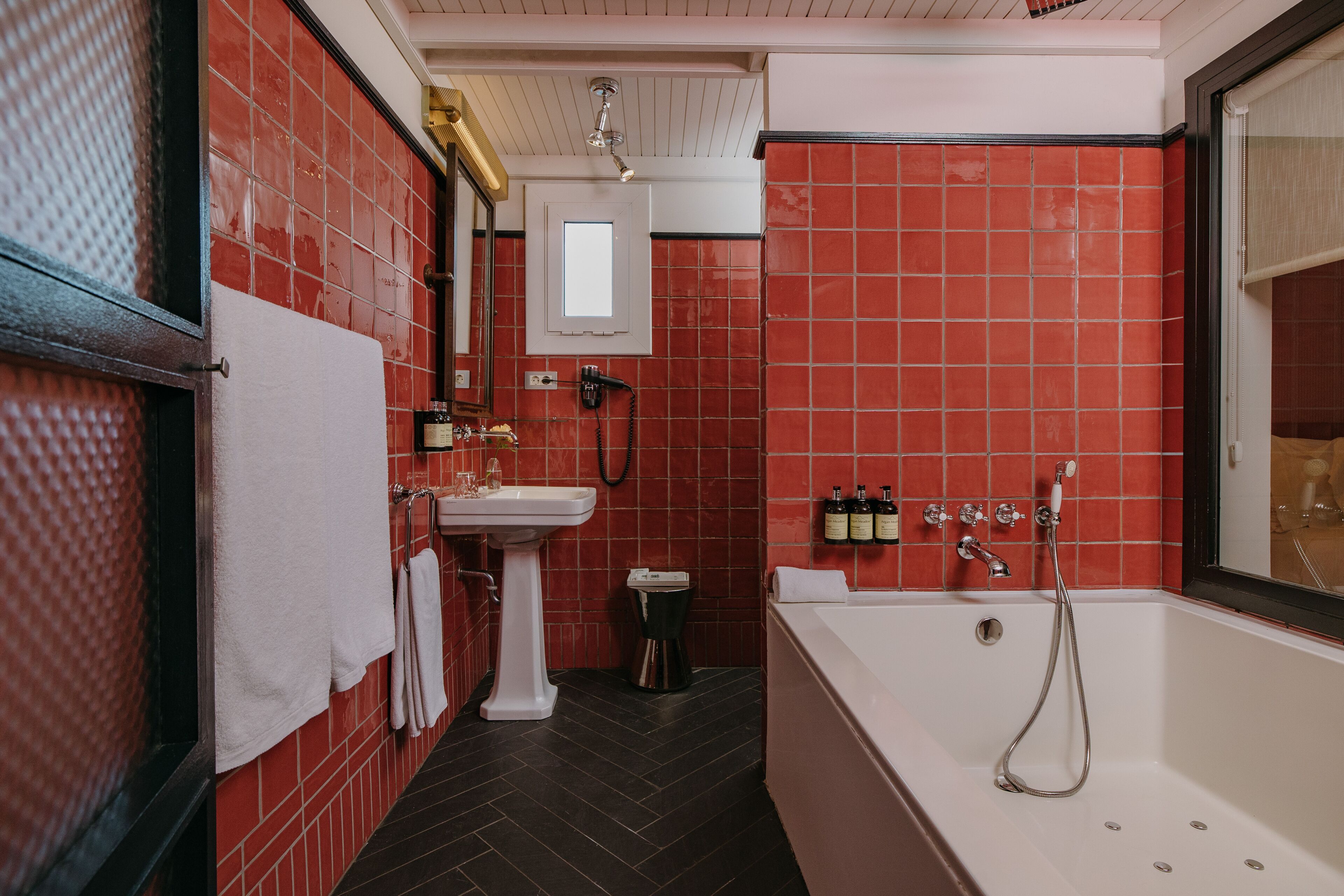Ein Badezimmer mit roten Fliesenwänden, einem weißen Waschbecken, einer Badewanne und einem Spiegel.
