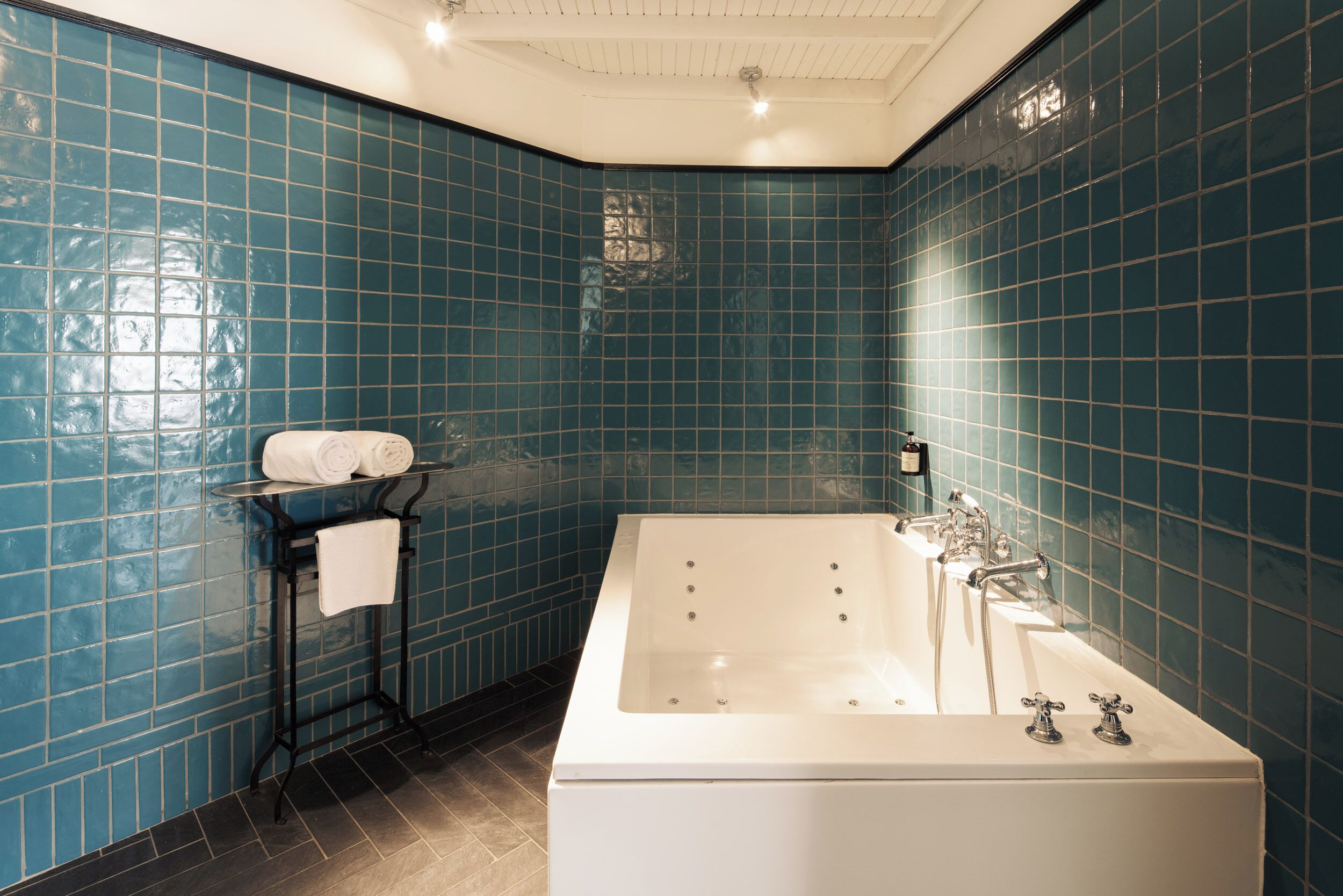 Un baño con una bañera grande, un perchero con toallas dobladas y paredes de azulejos azules.