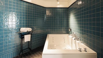 Een badkamer met een groot bad, een handdoekrek met opgevouwen handdoeken en blauwe betegelde wanden.