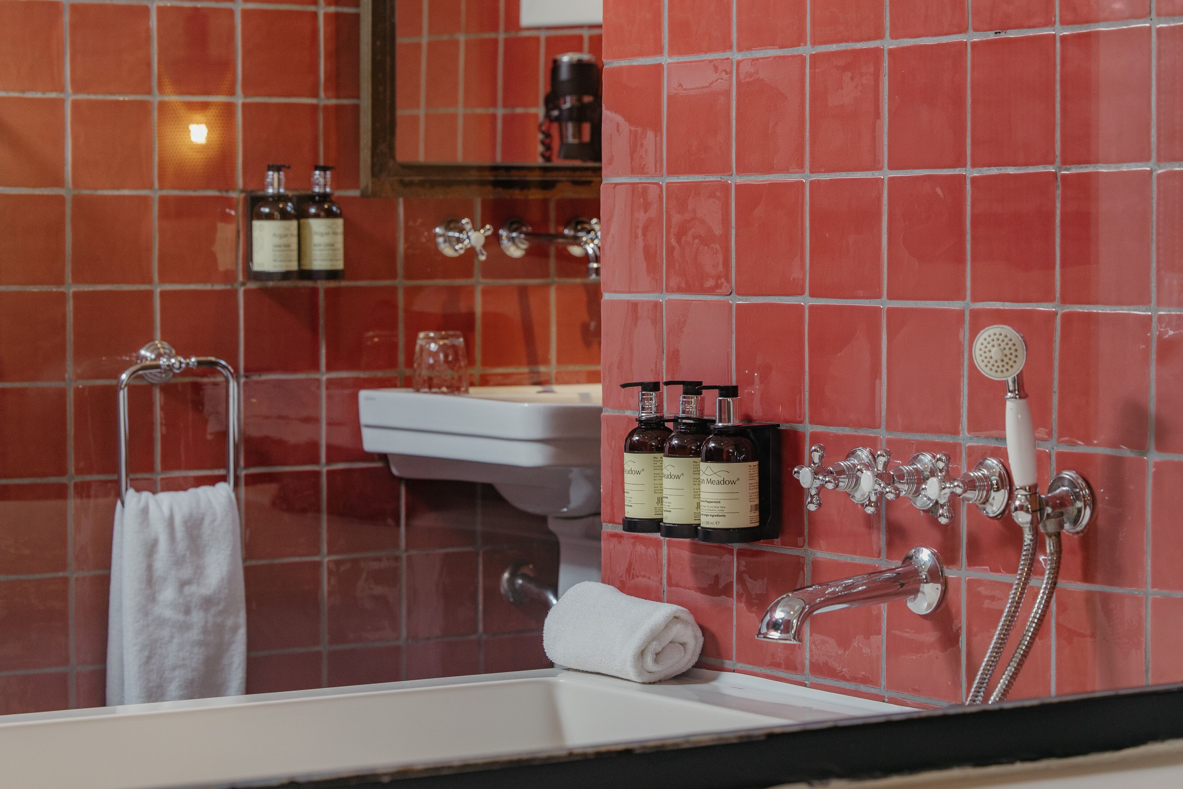 A bathroom with a red-tiled wall, a white sink, a towel rack, and a shower with a handheld showerhead.