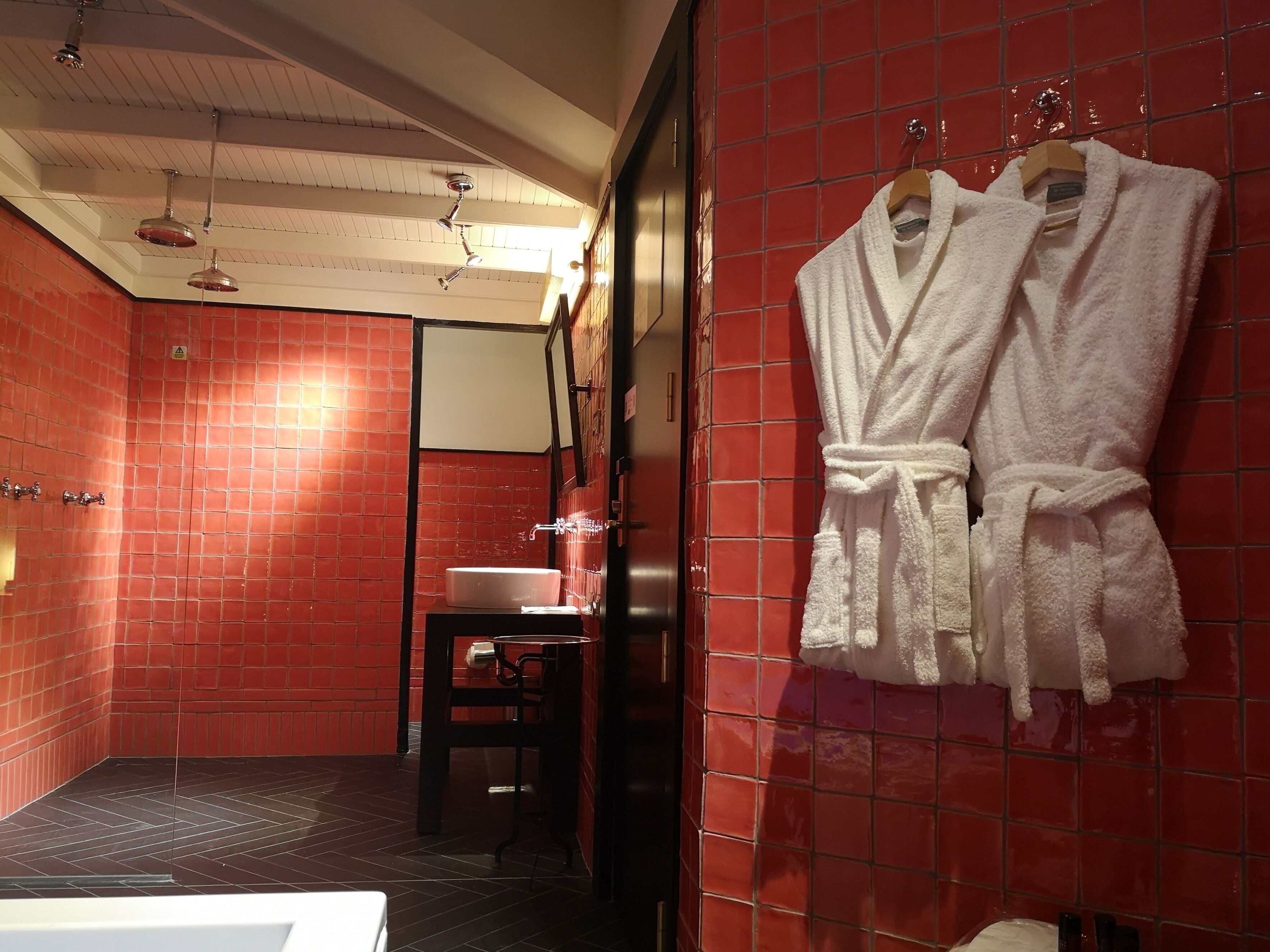 A bathroom with red tiled walls, a white sink, a mirror, and a white bathrobe hanging on the wall.
