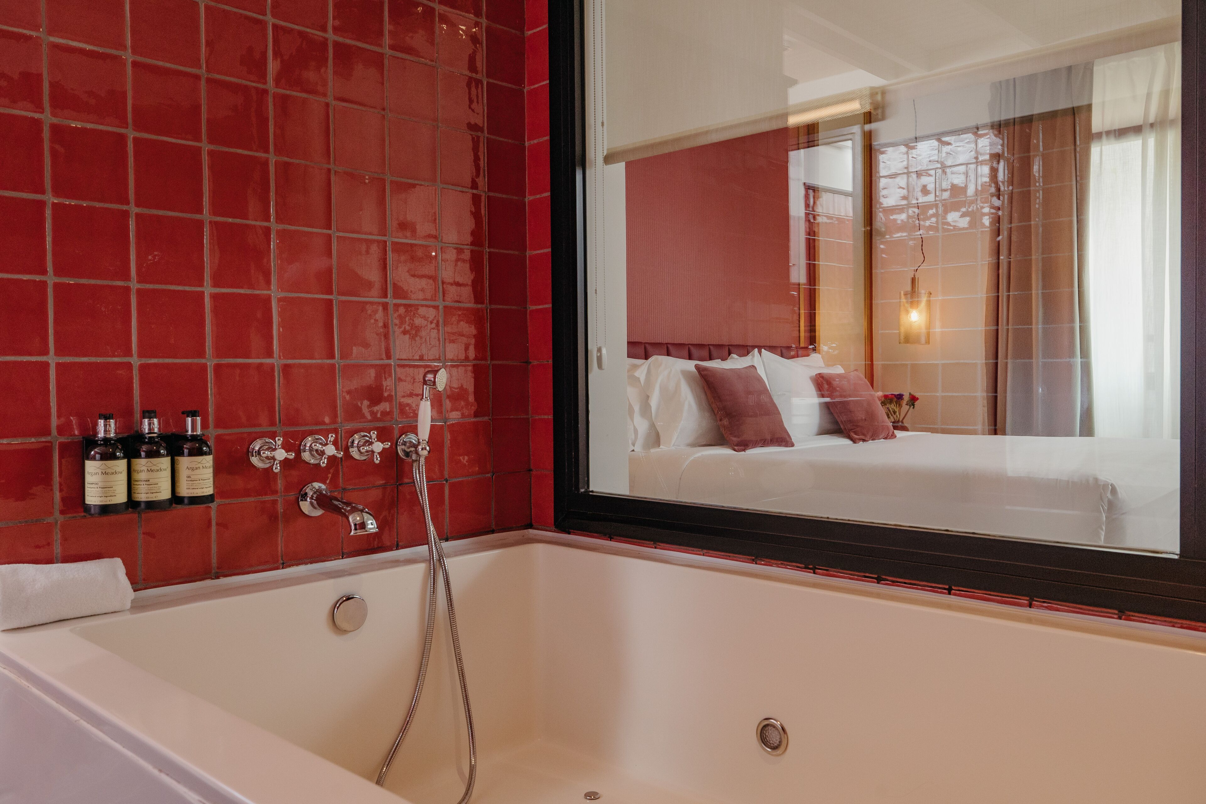 Ein Badezimmer mit Badewanne, Dusche und Spiegel, der ein Schlafzimmer mit Bett und Kissen reflektiert.