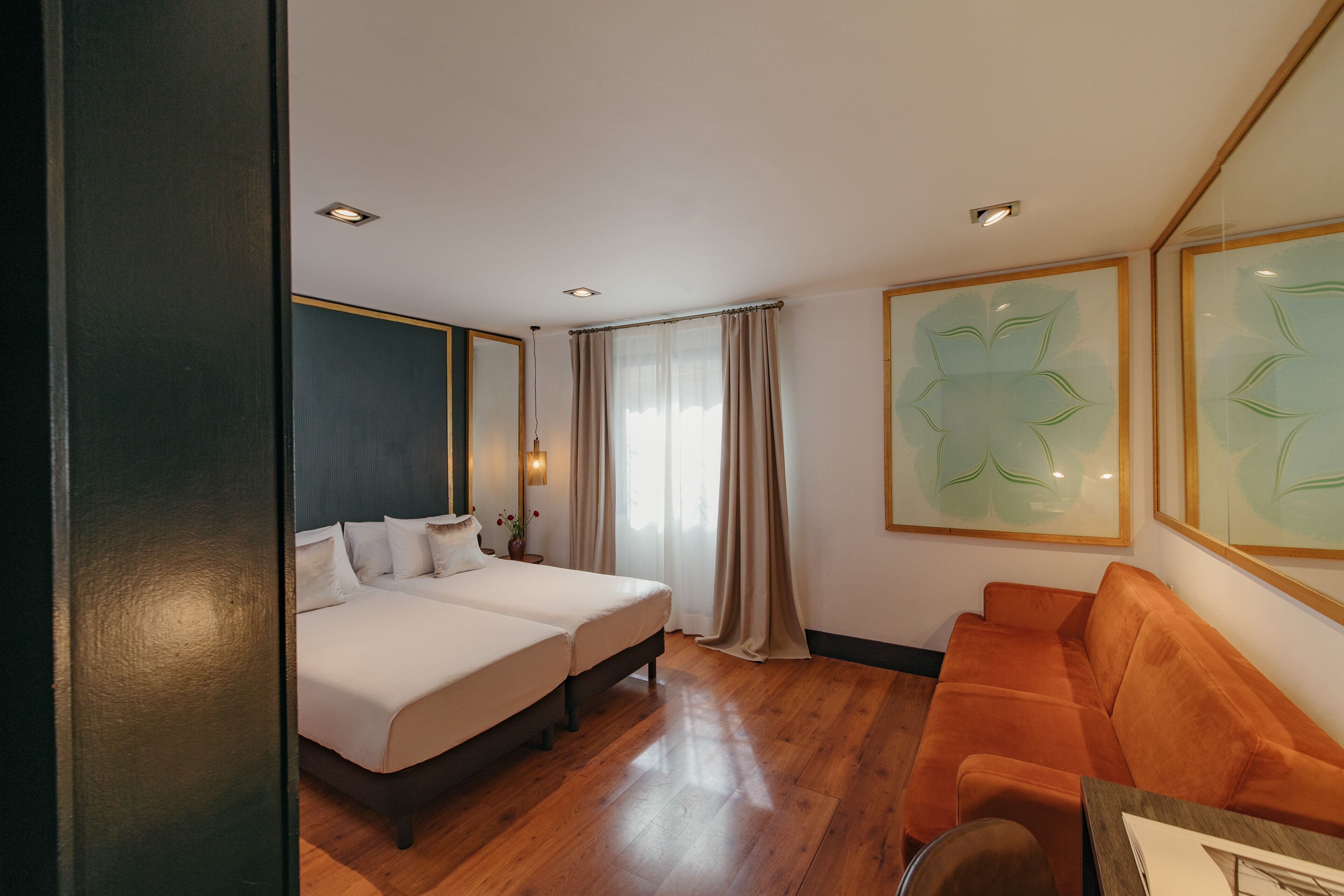 A hotel room with two beds, a sofa, and a large window with curtains.