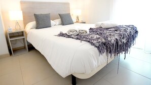 A neatly made bed with a white duvet, two pillows, and a textured throw blanket. There are two bedside tables with lamps and a power outlet. - La Lonja Homes - Turismo de Interior (Palma de Mallorca)