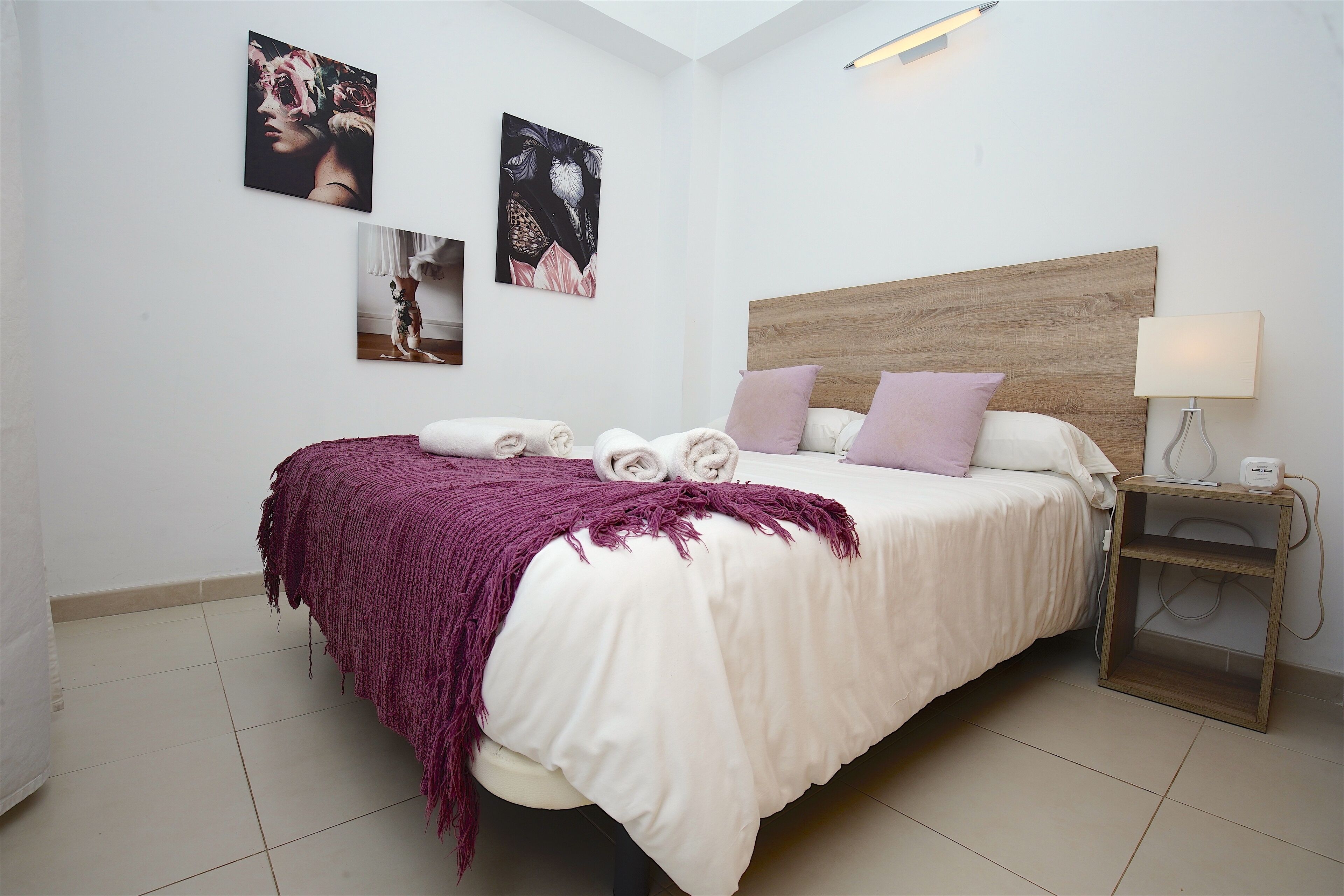 A bedroom with a bed, pillows, a blanket, and artwork on the wall.