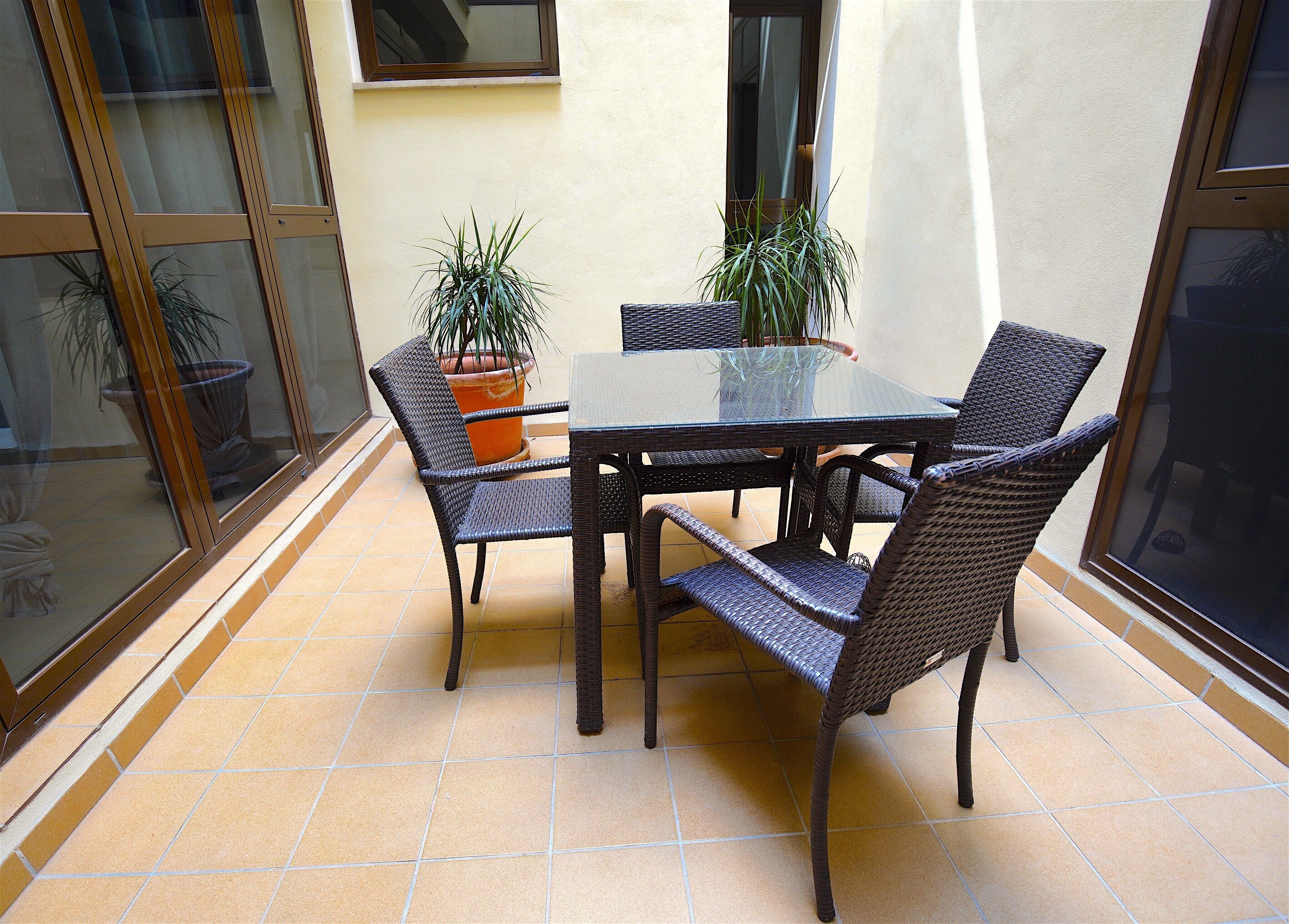 A glass-enclosed patio with a table and chairs, potted plants, and a view of the interior.