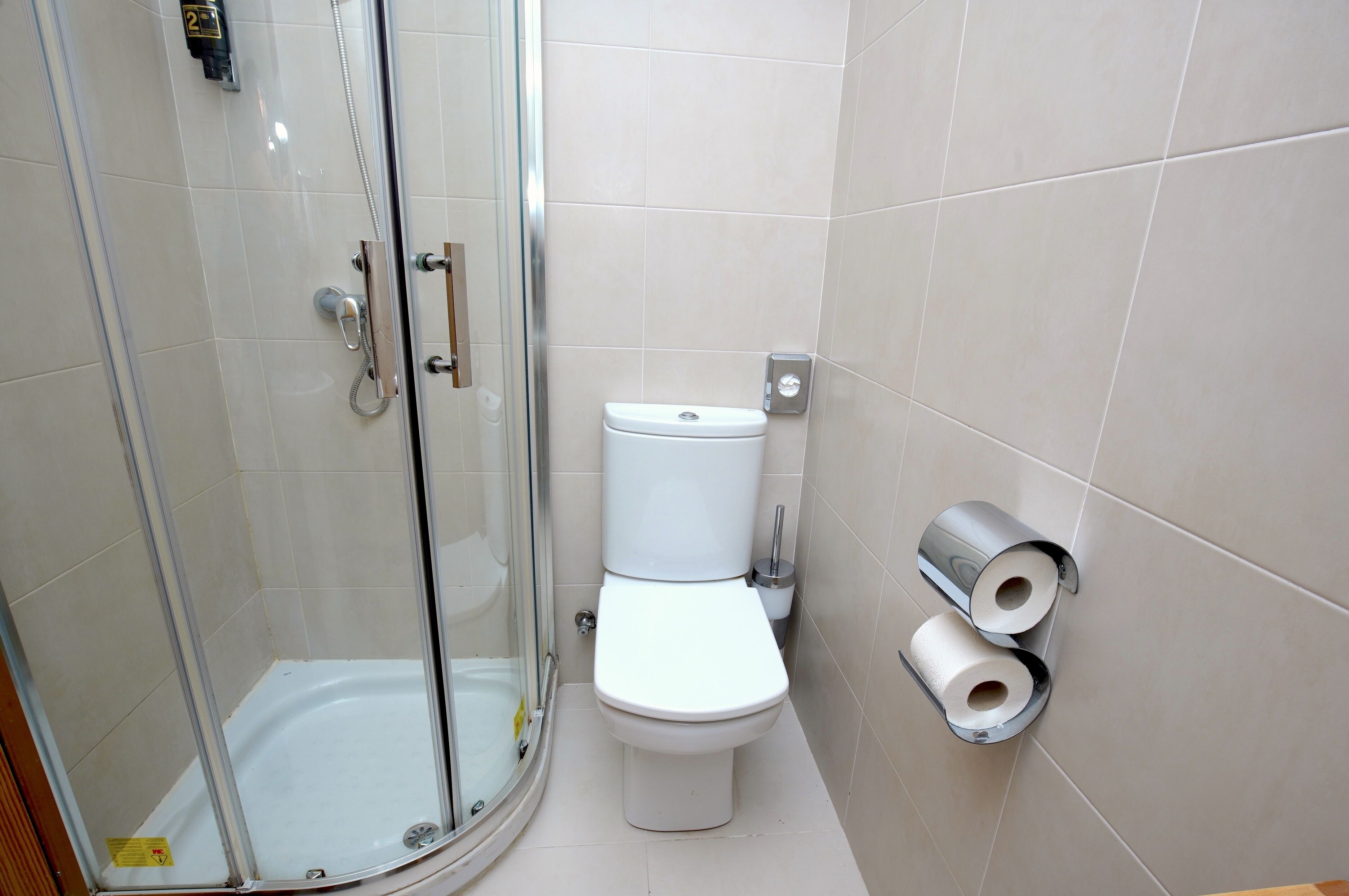 A bathroom with a glass-enclosed shower, a toilet, and two toilet paper holders on the wall.