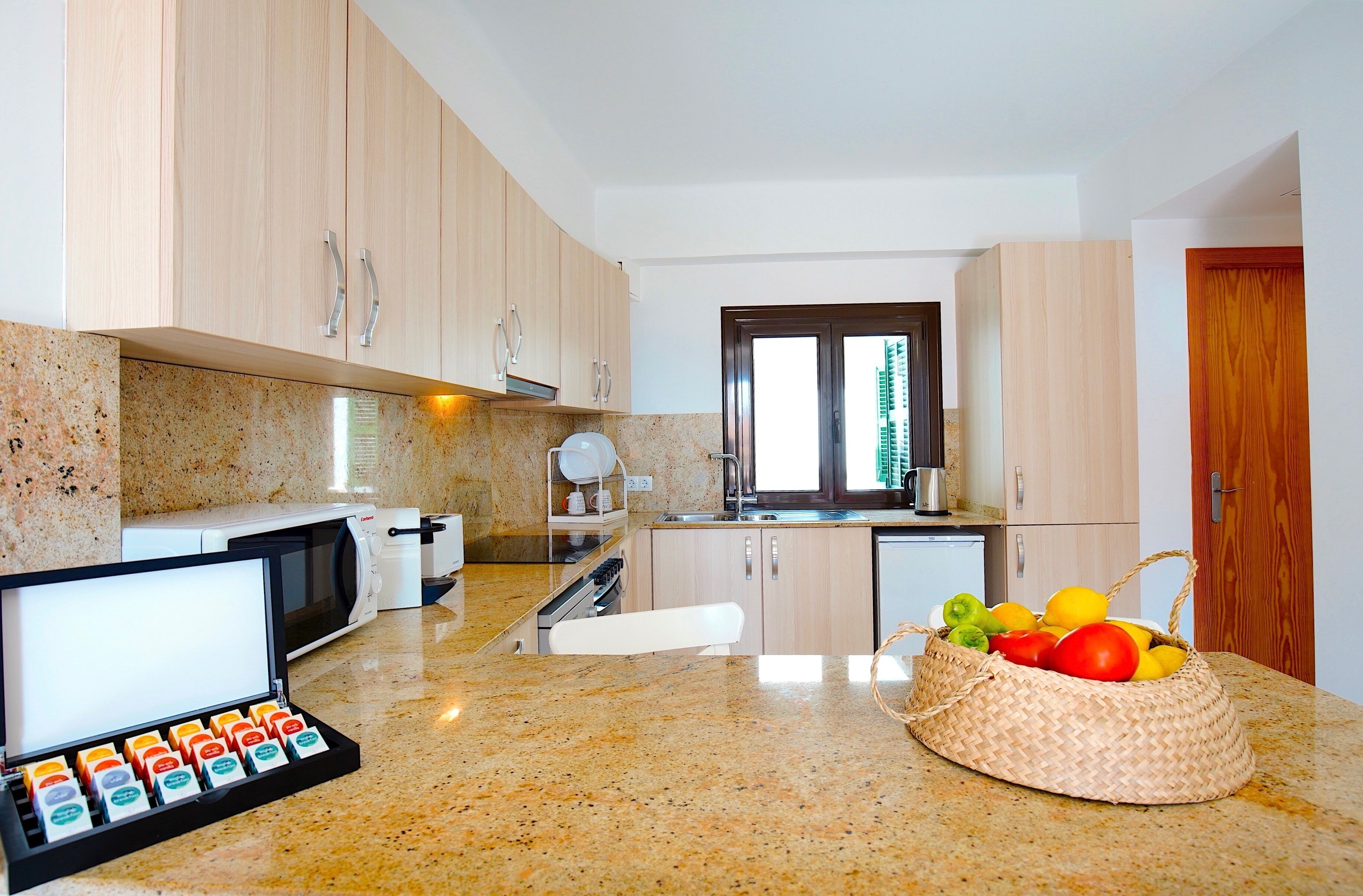Een moderne keuken met houten kastjes, een granieten aanrecht, een magnetron, een waterkoker en een mand met fruit.