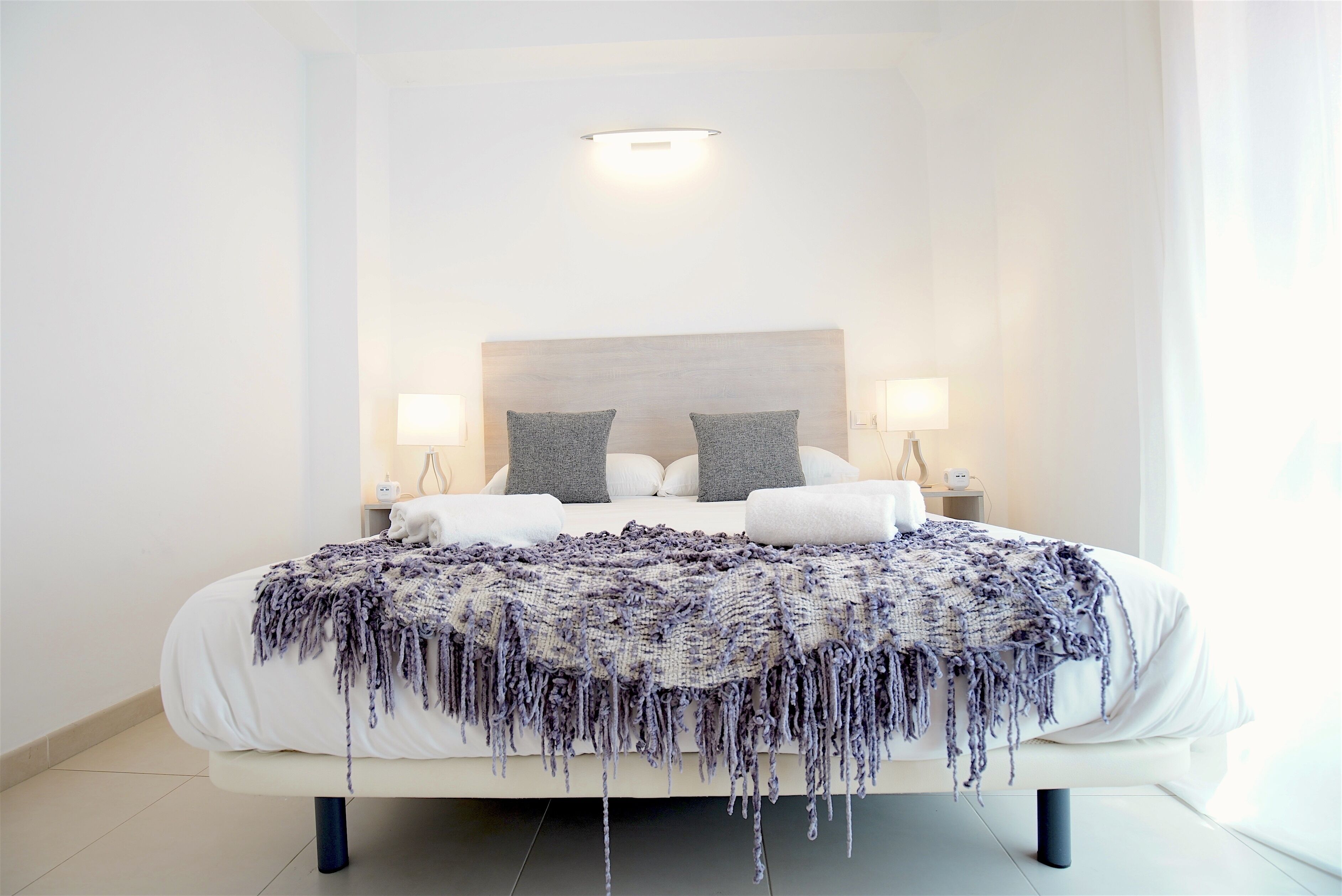 A modern bedroom with a large bed, two bedside tables with lamps, and a headboard with a light fixture.