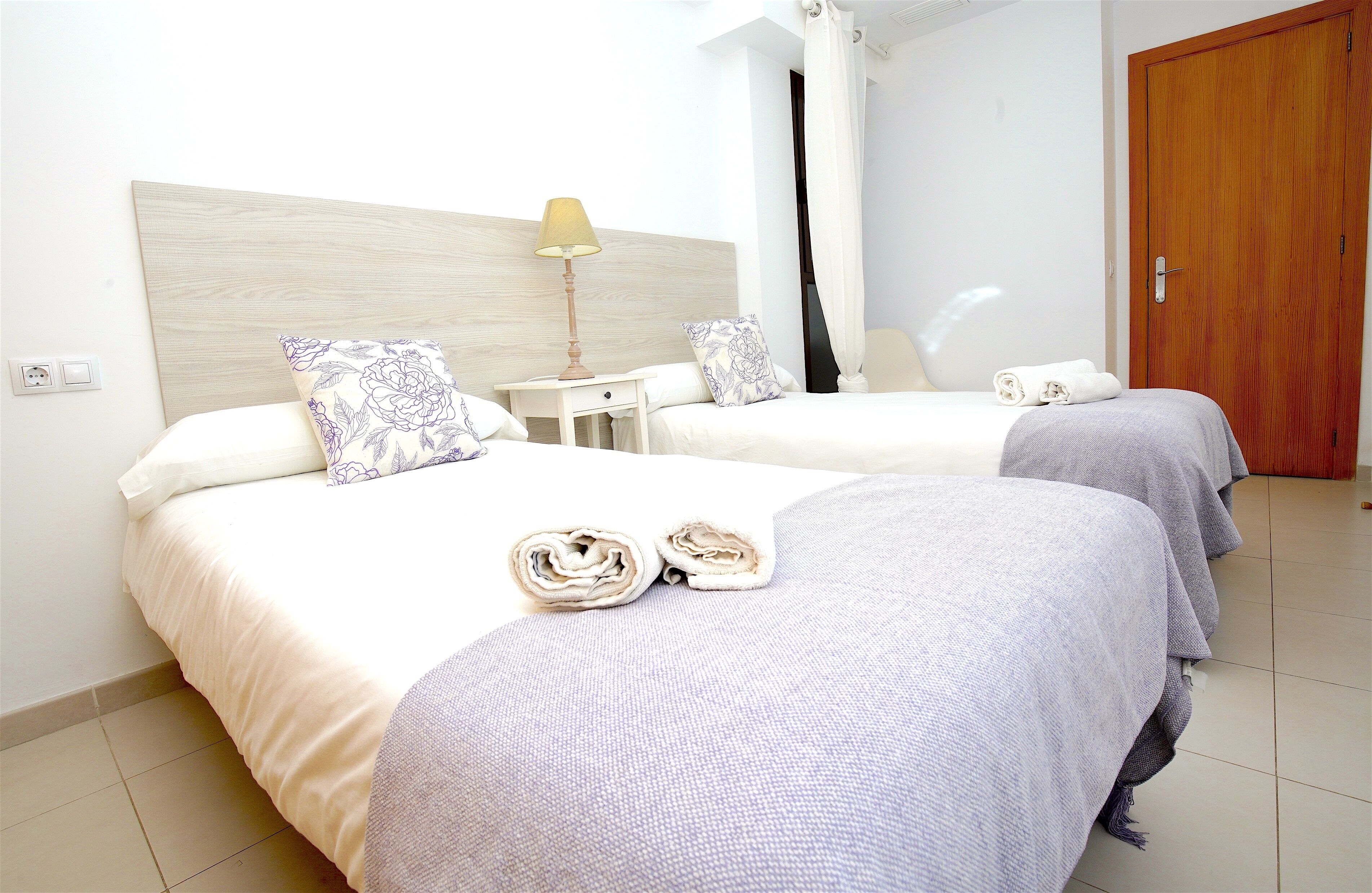 A hotel room with two beds, a nightstand with a lamp, and a wooden door.