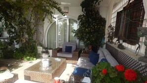Un espace extérieur lumineux, aménagé pour se détendre, avec une table à plateau de verre, des canapés confortables et une variété de plantes en pot.