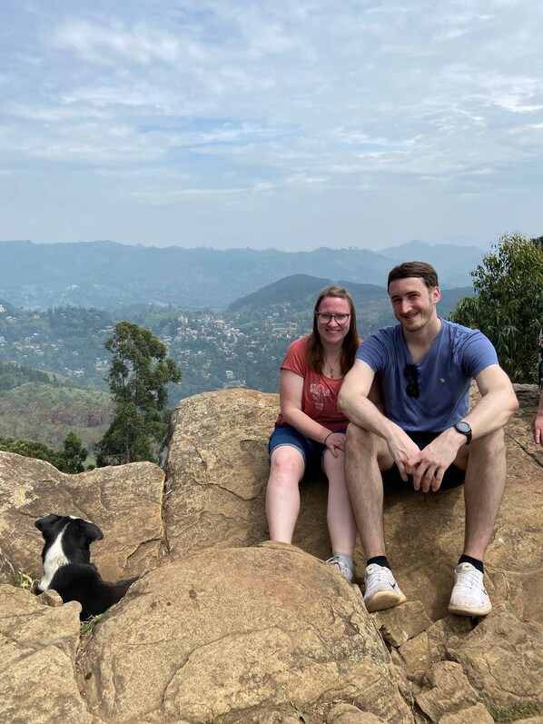 Dos personas sentadas sobre una roca, con vista a un valle y montañas al fondo.