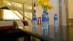 Een kamer met een bed, een tafel met waterflesjes en een vaas met gele bloemen.