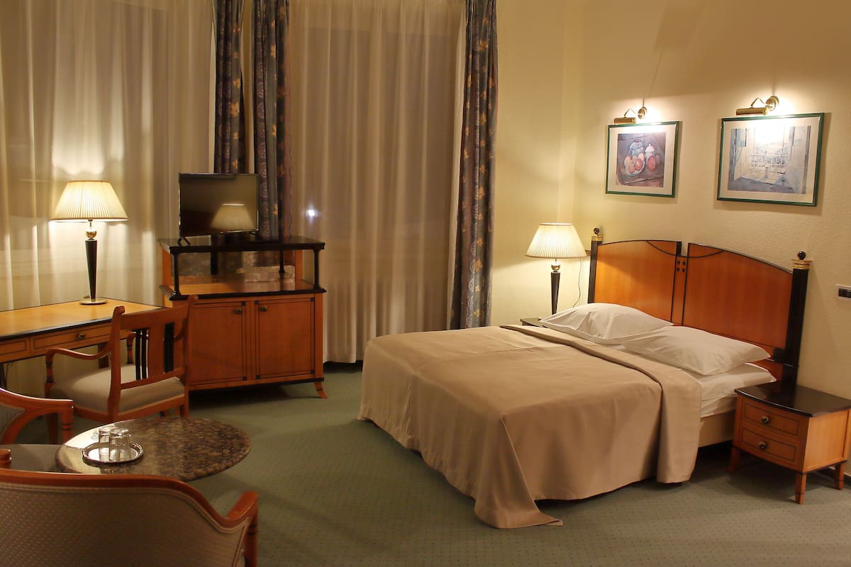 Quarto de hotel com cama, escrivaninha, cadeira, televisão e duas luminárias.